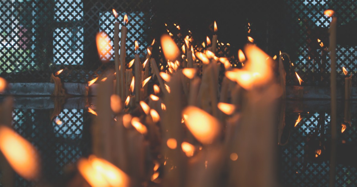 Tientallen brandende kaarsen in het donker, met warme vlammen tegen een donkere achtergrond.